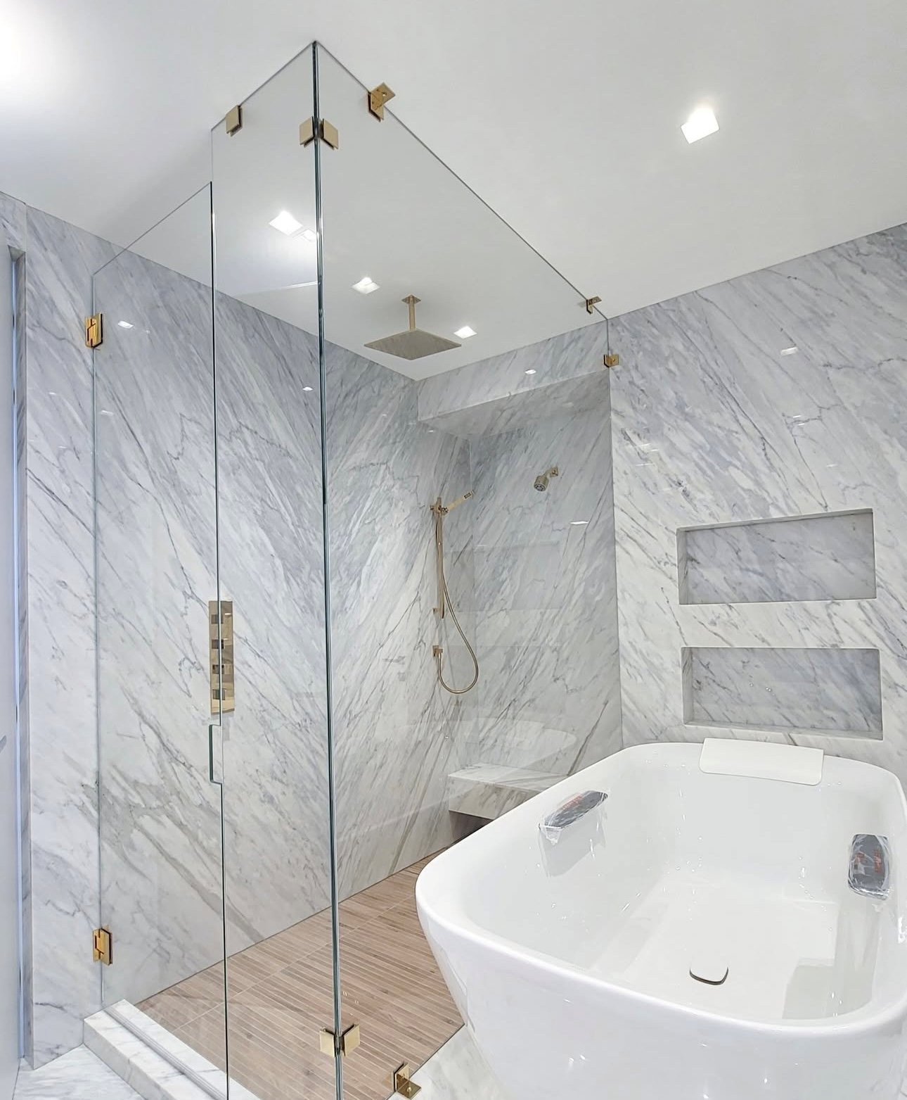 Mitered frameless glass shower corner with brushed gold hardware and marble walls