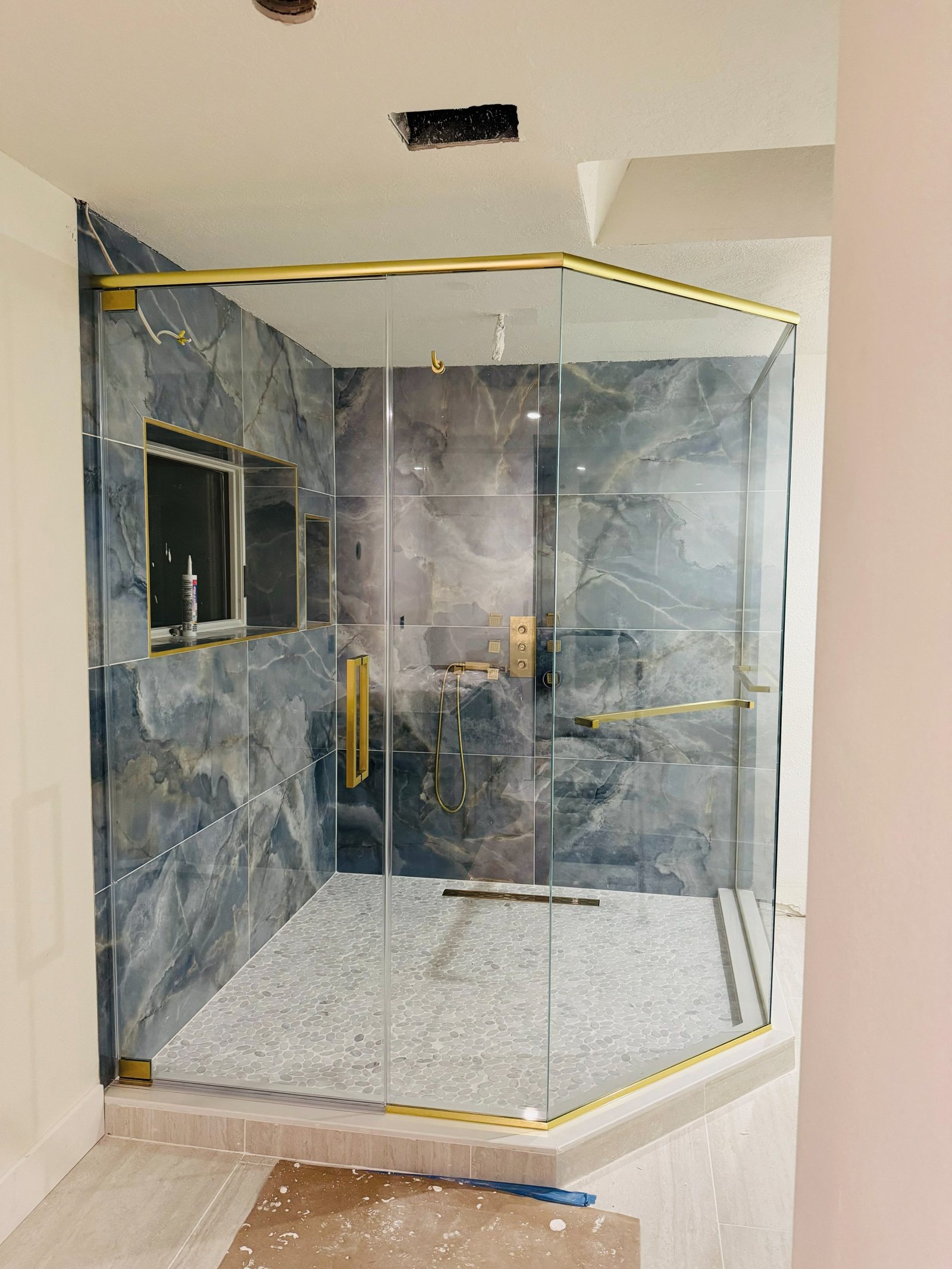 Frameless corner glass shower with brushed gold hardware and blue-grey marble walls