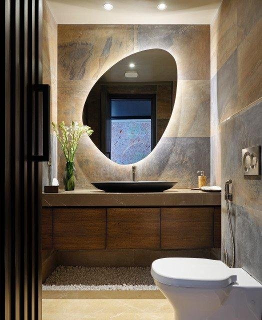 Custom organic-shaped backlit LED mirror in a stone powder room